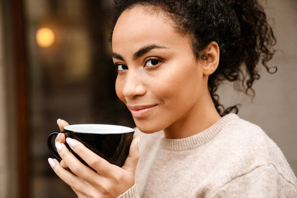 Young black woman smiling and drinking coffee in cafe outdoors - Photo, image
