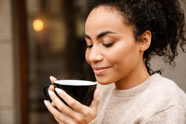 Young black woman smiling and drinking coffee in cafe outdoors - Photo, Image