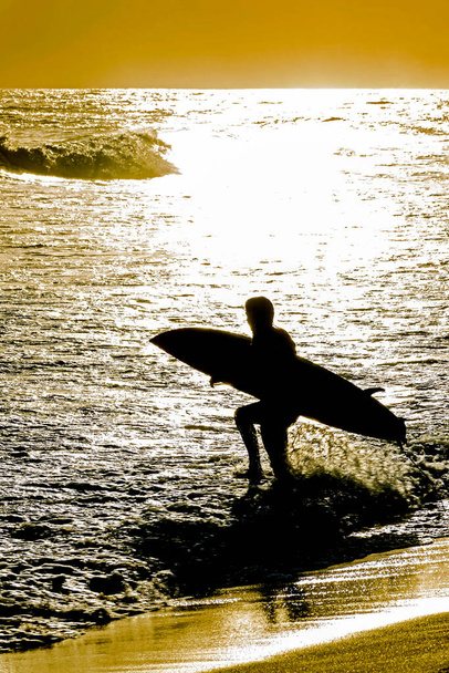 Siluetti surffaaja tulee mereen hänen surffilauta auringonlaskun aikana Ipanema rannalla Rio de Janeiro - Valokuva, kuva