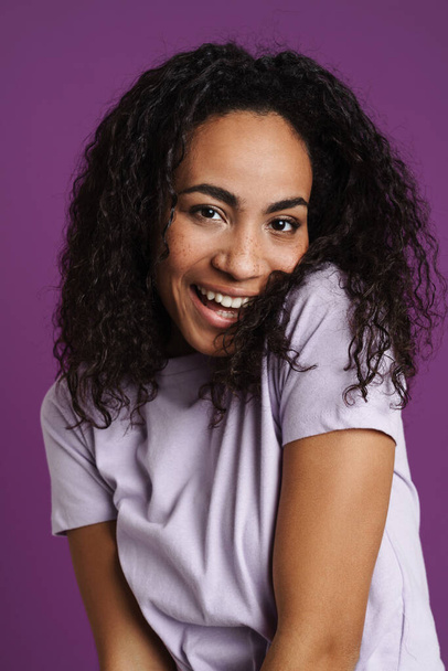 Молода чорна жінка з хвилястим волоссям сміється і дивиться на камеру ізольовано на фіолетовому фоні
 - Фото, зображення