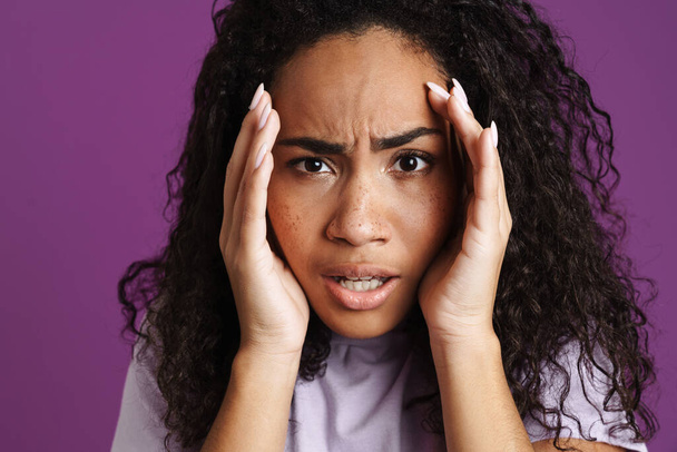 Young black woman with wavy hair expressing surprise at camera isolated over purple background - Photo, image