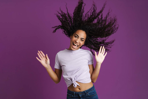 Молодая черная женщина с волнистыми волосами смеется над камерой, изолированной на фиолетовом фоне - Фото, изображение