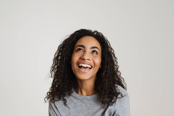 Young black woman with wavy hair laughing and looking upward isolated over white background - Foto, imagen