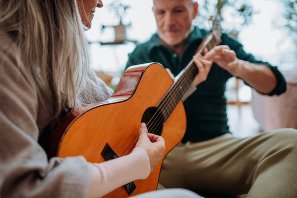 Старшая пара играет на гитаре, сидит в уютной гостиной и наслаждается осенним днем. - Фото, изображение