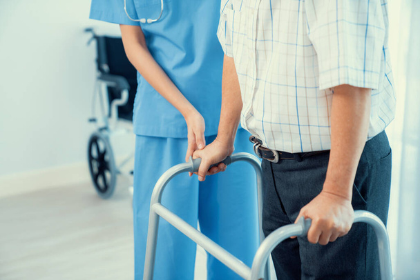 Physiotherapist assists contented senior man on folding walker. Recuperation for elderly, seniors care, nursing home. - 写真・画像