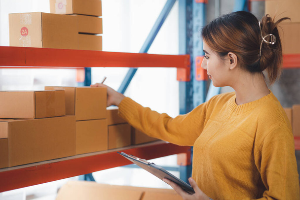 The owner of an online store is checking orders for packaged products in order to prepare them for delivery to customers as ordered through the website. Online selling and online shopping concepts. - Φωτογραφία, εικόνα