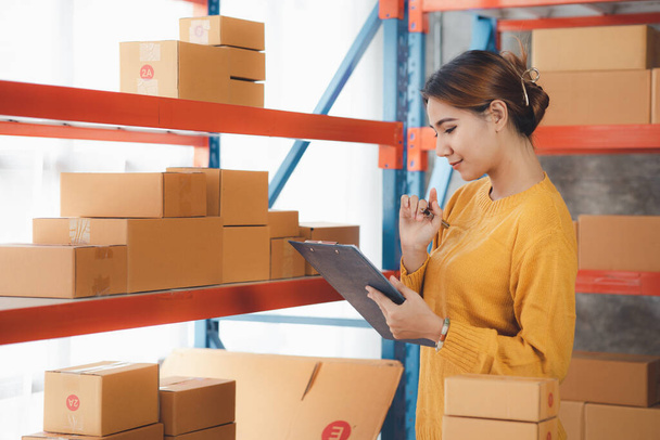 The owner of an online store is checking orders for packaged products in order to prepare them for delivery to customers as ordered through the website. Online selling and online shopping concepts. - Foto, Bild