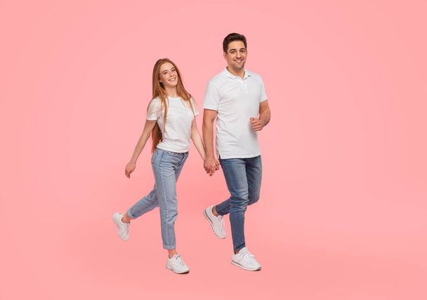 Full body of young man and woman in matching outfits of denim and white t shirt holding hands in pink studio - 写真・画像