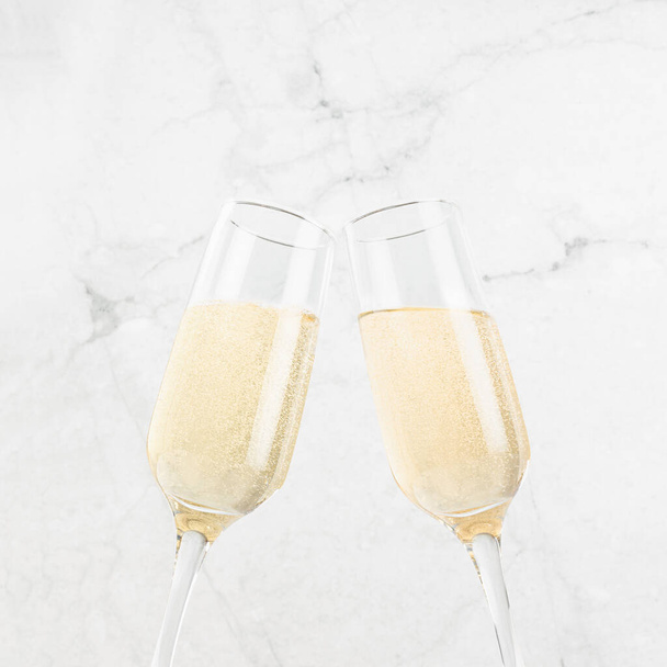 Fresh sparkling golden champagne in glasses in cheer and toast gesture and motion on elegant white marble backdrop with festive refreshing beverage in summer sunlight, top part, square.  - Fotografie, Obrázek