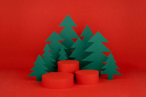 Christmas background with three cylinder podiums and scene with 3d rendering for presentation gifts, cosmetics, goods in red color with green spruce forest. New year template for advertising. - Fotografie, Obrázek