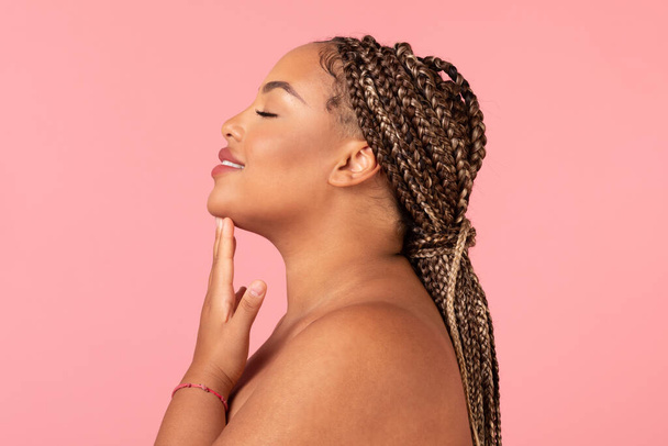 Facial treatment. Profile portrait of beautiful black obese woman with perfect skin touching her chin over pink studio background with copy space, side view - Foto, immagini