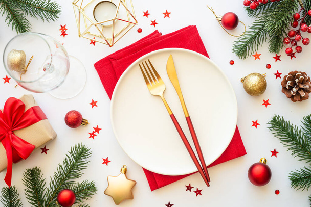 Cibo natalizio, tovaglia natalizia con piatto bianco, posate dorate e decorazioni natalizie su sfondo bianco. Vista dall'alto. - Foto, immagini