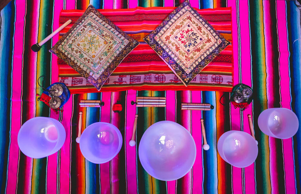 Große Quarz-Klangschalen, Glockenspiel-Glocken und Tingsha-Becken über einem andinen (peruanischen) Handgewebe mit violettem Licht - Foto, Bild