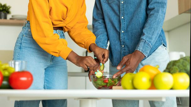 Wizerunek afrykańskich małżonków gotujących zdrowe wegetariańskie jedzenie w kuchni, czarna para przygotowująca sałatkę warzywną na obiad, panorama, zbliżenie - Zdjęcie, obraz