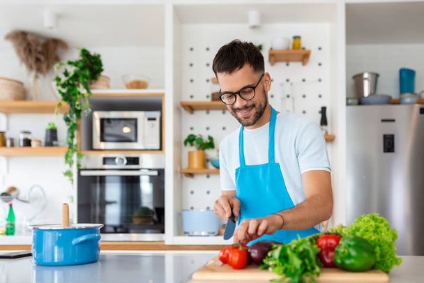 Fešák mladý muž stojí u moderní kuchyně sekané zeleniny připravit čerstvý zeleninový salát k večeři nebo obědu, mladý muž vaření doma, aby snídaně sledovat zdravou stravu, vegetariánský koncept - Fotografie, Obrázek