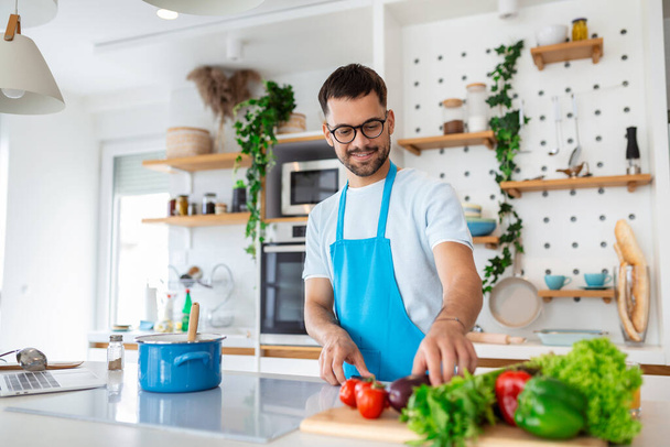 Красивый молодой человек стоять на современной кухне отбивные овощи подготовить свежий овощной салат на ужин или обед, молодой мужчина приготовления пищи на дому сделать завтрак следовать здоровой диеты, вегетарианская концепция - Фото, изображение