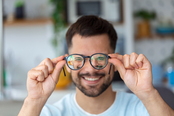 молодой африканский мужчина держит очки с диоптриевыми линзами и смотрит через них, проблема близорукости, коррекции зрения - Фото, изображение