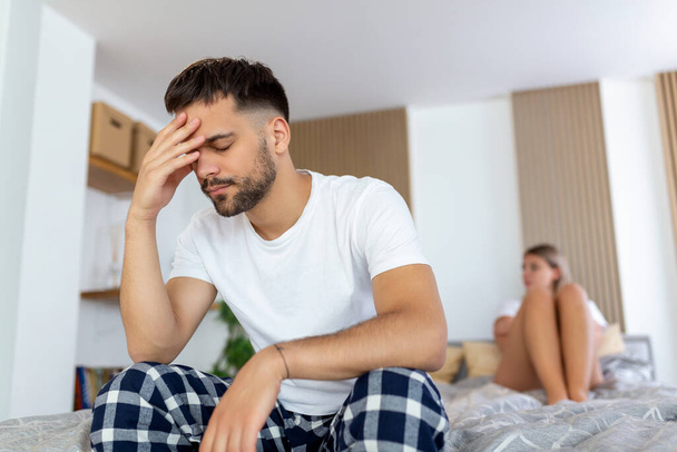 Mladý smutný muž sedí na posteli a hádá se s manželkou. hotel, cestování, vztahy, a sexuální problémy koncept - rozrušený muž sedí na posteli se ženou na zádech - Fotografie, Obrázek