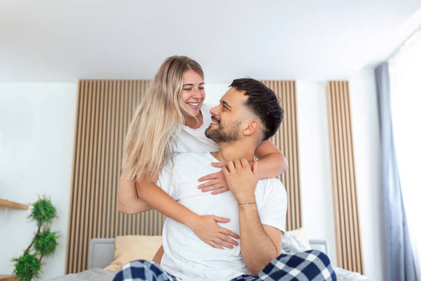 Portrait of young couple sitting on bed and look at each other. Attractive beautiful new marriage man and woman in pajamas enjoy morning activity in bedroom at home. Family relationship concept. - Photo, Image