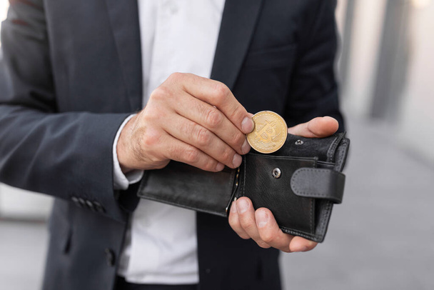 Young european male ceo manager with beard in suit puts bitcoin coin in wallet, enjoy investment and profit on city street, cropped. Saving new cryptocurrency, finance and startup, modern business - Fotografie, Obrázek