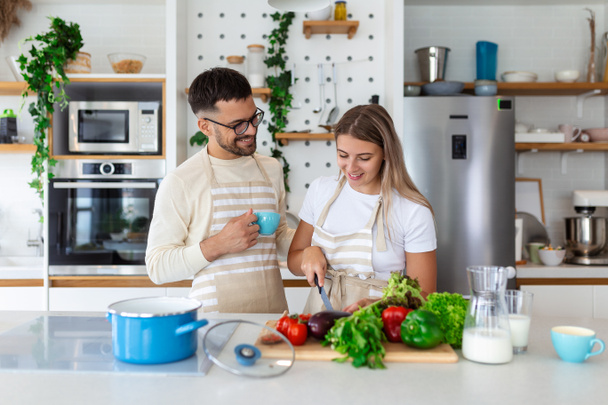 Porträt eines glücklichen jungen Paares, das zu Hause gemeinsam in der Küche kocht. romantisch Attraktive junge Frau und gutaussehender Mann genießen die gemeinsame Zeit, während sie auf der hellen modernen Küche stehen. - Foto, Bild