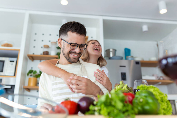 onnellinen nuori pari pitää hauskaa modernissa keittiössä sisätiloissa valmistellessaan tuoreita hedelmiä ja vihanneksia ruokasalaattia. Kaunis nuori pari puhuu ja hymyilee ruoanlaitossa terveellistä ruokaa kotona. - Valokuva, kuva