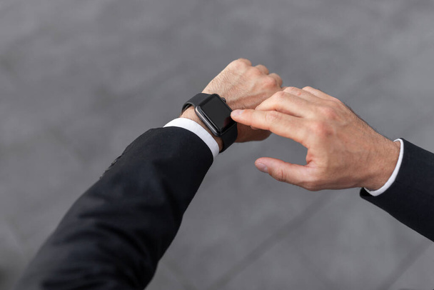 Hand of young european man in suit looks at clock, waiting for meeting at city street, cropped, close up, pov. Urban lifestyle, punctuality for work, finance and startup, time for modern business - Photo, Image