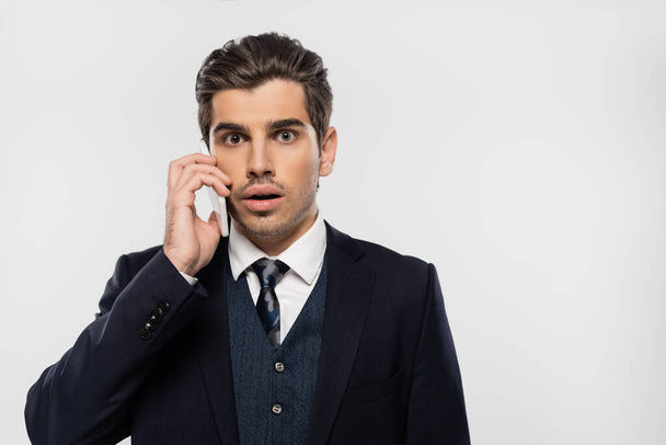 sorprendido hombre de negocios en traje hablando en teléfono inteligente aislado en gris - Foto, Imagen