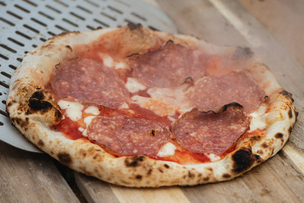 Domates soslu sıcak pizza, mozzarella ve tahta tahtada kürekle salam eti servis etmek. - Fotoğraf, Görsel