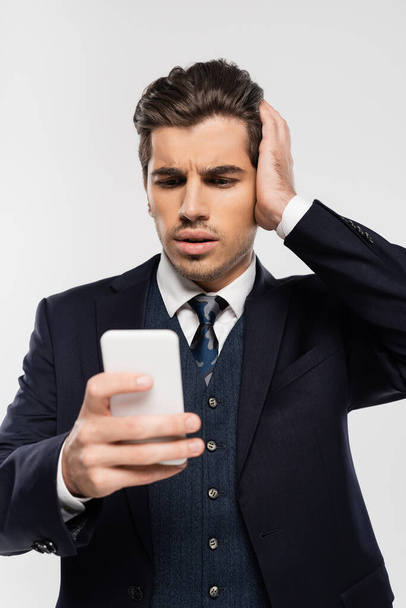 worried businessman in suit messaging on smartphone isolated on grey - Fotó, kép