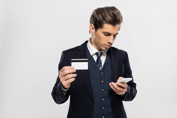 Takım elbiseli iş adamı akıllı telefon kullanıyor ve gri üzerinde kredi kartı tutuyor. - Fotoğraf, Görsel