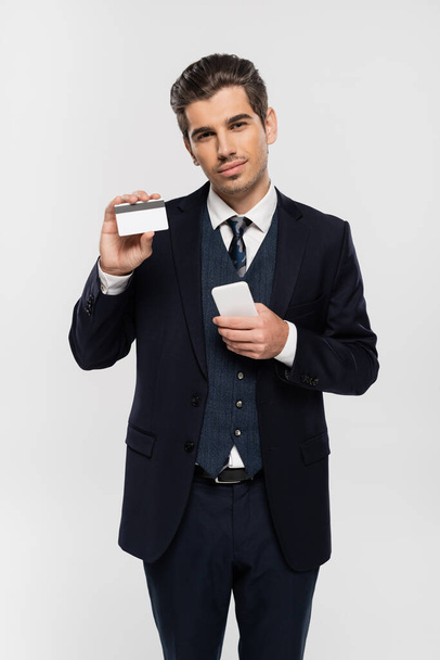 young businessman in suit holding smartphone and credit card isolated on grey  - Foto, immagini