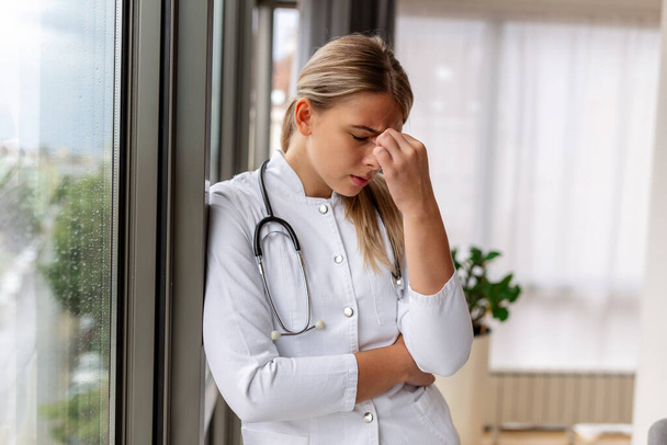 Young doctor looking distressed. Tired exhausted female doctor in uniform at hospital holding her head. Depressed sad doctor feels burnout stress - Foto, immagini