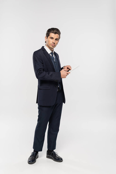 full length of young businessman in suit holding digital tablet on grey  - Fotoğraf, Görsel