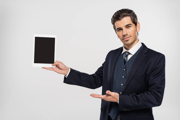 young businessman in suit pointing at digital tablet with blank screen isolated on grey  - Photo, image