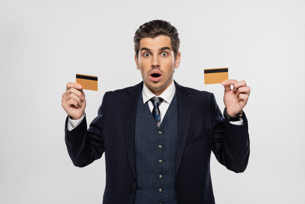 shocked businessman in suit holding credit cards isolated on grey - Fotoğraf, Görsel