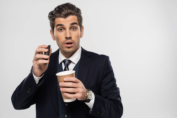 surprised and sleepy businessman holding paper cup with takeaway drink isolated on grey - Foto, imagen