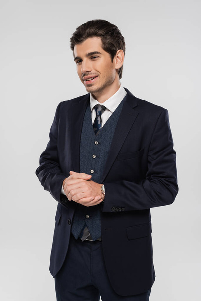 cheerful businessman in formal wear smiling and standing with clenched hands isolated on grey - Photo, Image