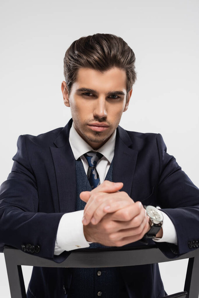 serious businessman with clenched hands sitting on chair isolated on grey - Photo, image