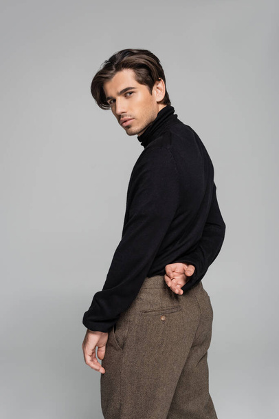 good looking man in black turtleneck and pants looking at camera isolated on grey - 写真・画像