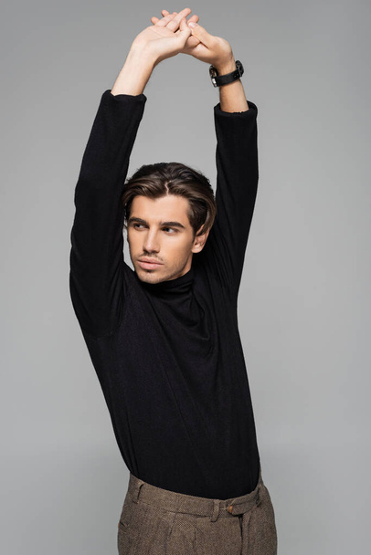 young good looking man in black turtleneck posing with raised hands isolated on grey - Фото, изображение