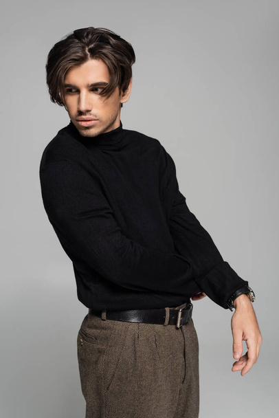 brunette young man in black turtleneck posing and looking away isolated on grey - Fotó, kép