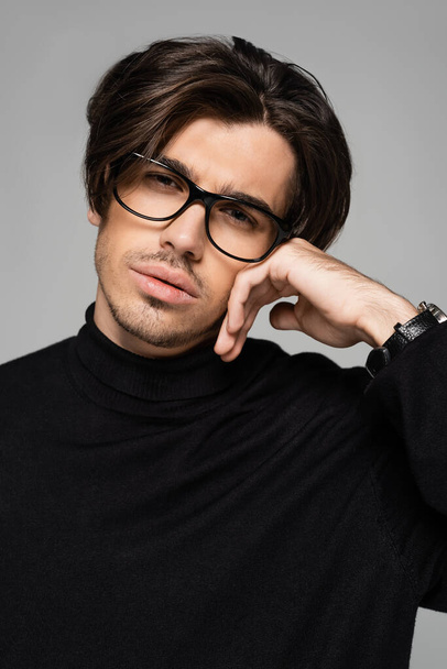 portrait of good looking man in black turtleneck and eyeglasses posing isolated on grey - Fotó, kép