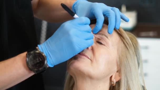 Megjelölni egy idős nő arcát egy plasztikai műtét előtt. Egy hivatásos plasztikai sebész megvizsgálja a beteget. - Felvétel, videó