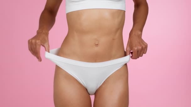 Successful slimming. Young fit unrecognizable woman demonstrating weightloss, showing big panties, pink studio background, slow motion - Footage, Video