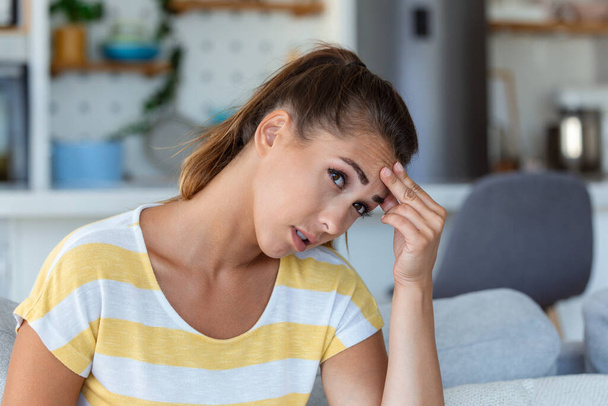 Päänsärky Lähikuva kuva nuori nainen, joka istuu sohvalla, koskettaa päätään kärsiessään migreeni. - Valokuva, kuva