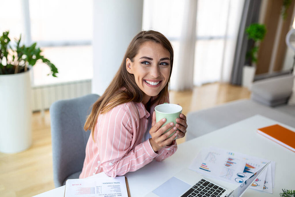 オフィスの若いビジネス女性はコーヒーを飲み、窓を通して見る - 写真・画像