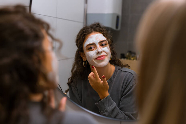 Young woman puts face mask in front of a mirror - Photo, image