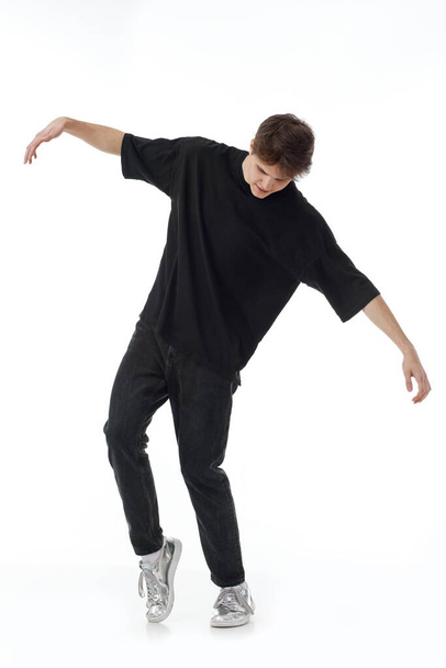 young man in black t-shirt and jeans dancing on white background. Full length - 写真・画像