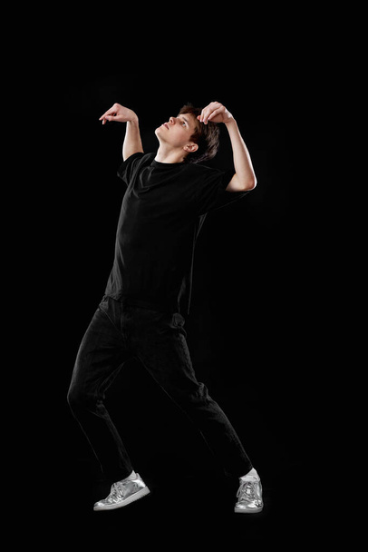 Młody mężczyzna w czarnej koszulce tańczący na czarnym tle. Pełna długość - Zdjęcie, obraz